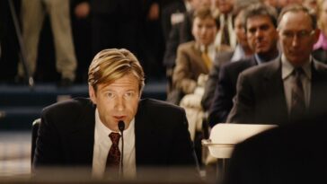 Nick Naylor (Aaron Eckhart) speaks into a microphone in a courtroom full of people in Thank You for Smoking