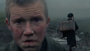 In this image from Come and See, the character Flyora, aged by his experience, stares in angusih at the camera while a young boy behind him carries a rifle and pack.