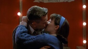 In this image from Dogfight, Eddie (River Phoenix) and Rose (Lili Taylor) embrace and kiss in front of a red backdrop.