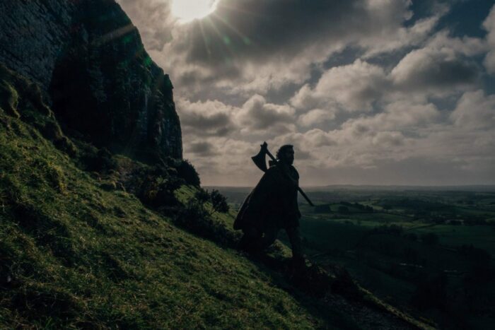 Gawain stands on a high cliff path with an axe on his shoulder.