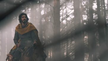 Gawain rides on horseback through a sunlight forest.
