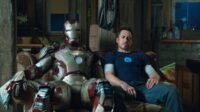 Tony Stark sits on a couch next to his disabled Iron Man armor