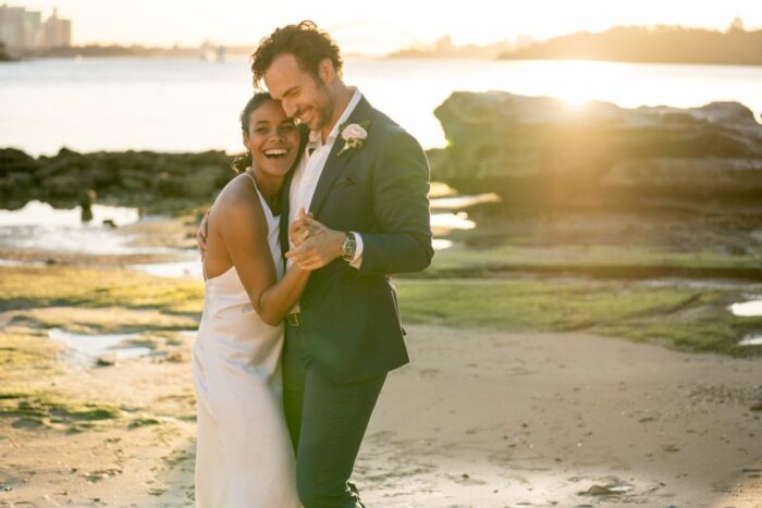 A pair of newlyweds embrace on a beach at sunset.