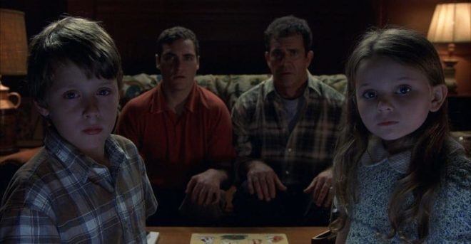 Morgan (Rory Culkin), Merrill (Joaquin Phoenix), Graham (Mel Gibson), and Bo (Abigail Breslin) stare in shock at their TV set as they watch news of a possible alien invasion.