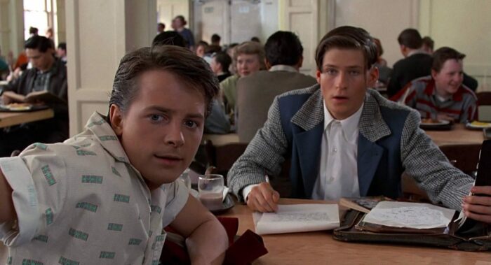 Marty McFly and his teenage father are sat in a school cafeteria watching an event off-screen (Back to the Future)