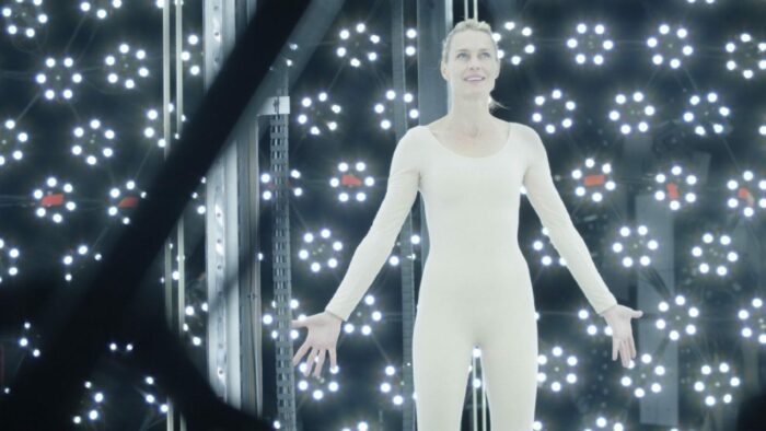 Robin Wright wears all white with her arms outstretched in front of a wall with circles of light on it