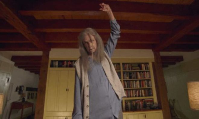 Nana (Deanna Dunagan) scarily stands in the middle of her living room looking possessed with her arm raised in the air and her eyes crossed.