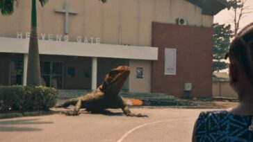 Screenshot from the Criterion Channel short film Lizard. Juwon has her back to us as she looks at a giant lizard in front of the church.