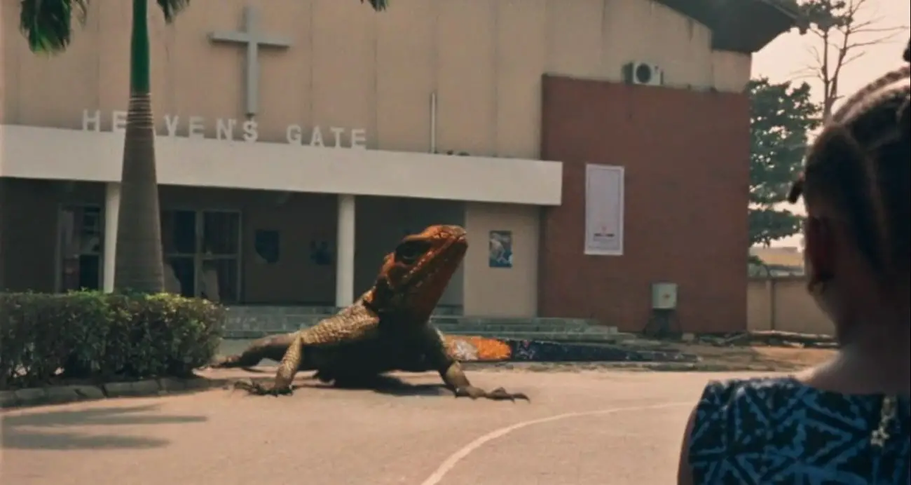 Screenshot from the Criterion Channel short film Lizard. Juwon has her back to us as she looks at a giant lizard in front of the church.
