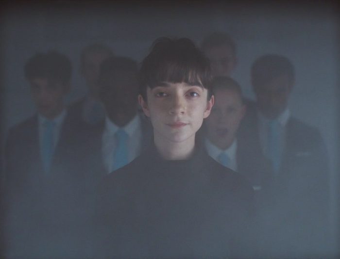 Screenshot from the Criterion Channel short film Devil's Harmony. Kiera stands in front of the choir in a hazy room.