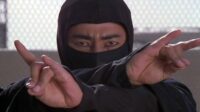 Cho, in ninja garb, crosses his arm in a stance.