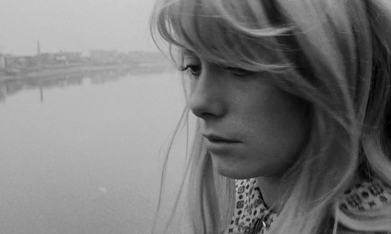 In this image from Repulsion, Carol (Catherine Deneuve) is depicted in close-up staring downward to her right with a river in the background.