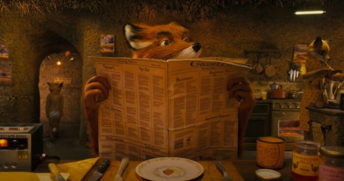 Mr. Fox looks up from reading the newspaper. He sits at the kitchen table. His wife cooks in the background on the right, and his son walks into a hallway on the left. Another example of Wes Anderson symmetrical framing.