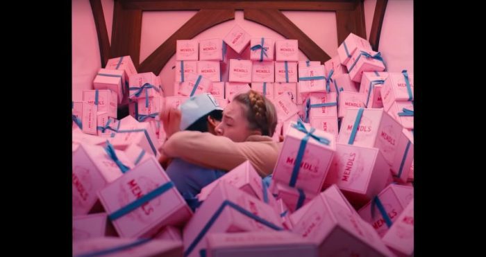 Zero and Agatha hug among pink boxes of pastries. The pastries are piled high around them, like a ball pit.
