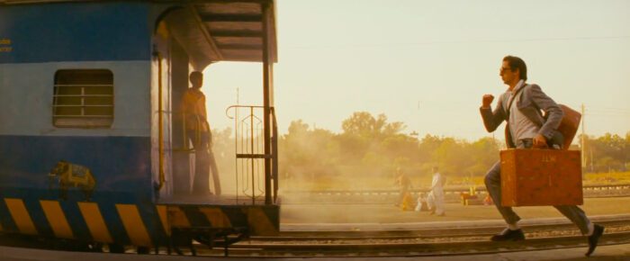 Adrien Brody runs to catch the train, suitcase in hand. The shot is an example of Wes Anderson's symmetrical framing of his shots, with the train on the left half of the right, and Brody on the right.