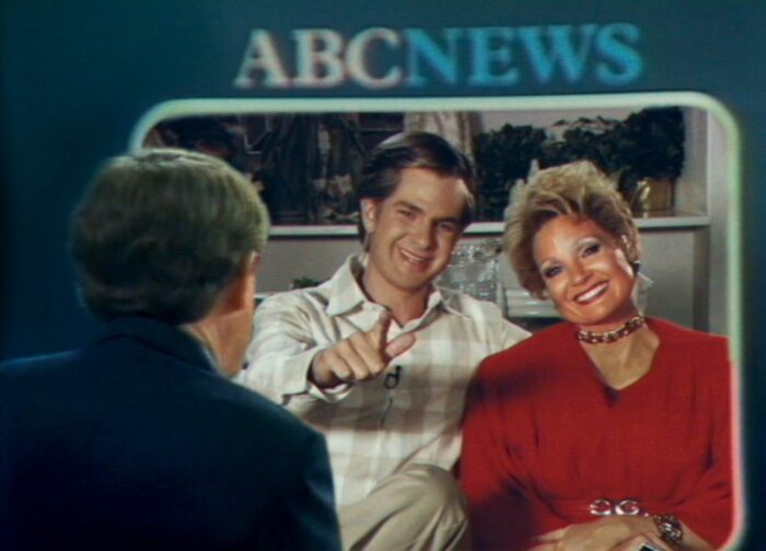 A television screen shows a couple talking to an interviewer.
