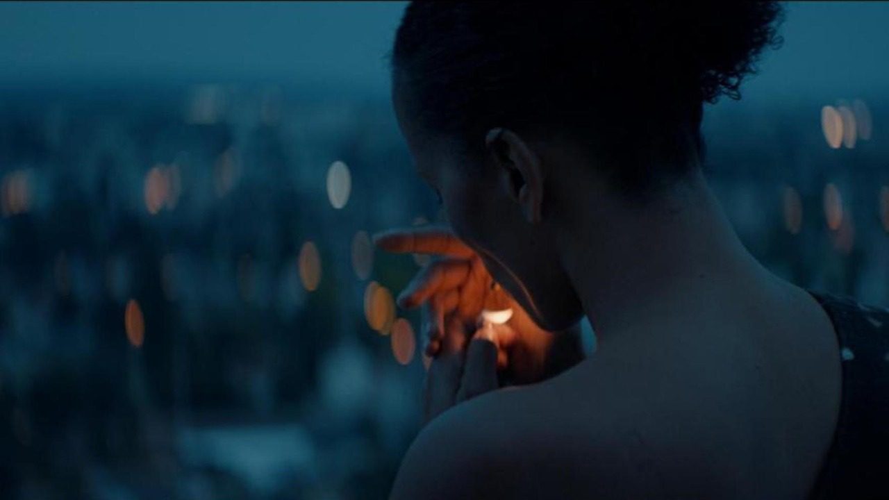 Emmanuelle (Clarissa Albrecht) lights a cigarette while surveying her new home city at night