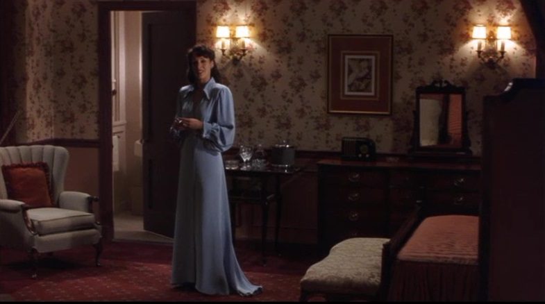 Image from Devil in a Blue Dress: Daphne Monet (Jennifer Beals) is depicted in a living room wearing a light blue floor-length dress.