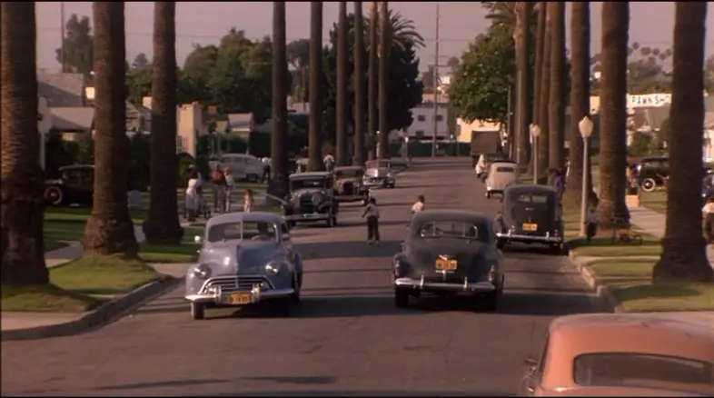 Image from Devil in a Blue Dress: cars pass and children play in a sunny African-American neighborhood.