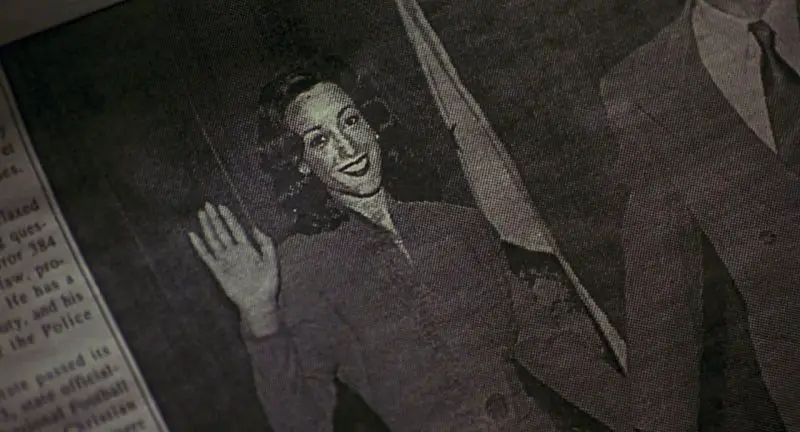 Image from Devil in A Blue Dress: a close-up of a newspaper photo depicts a smiling Daphne Monet (Jennifer Beals) waving to the cmaera.