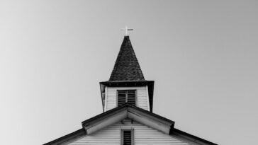 A church steeple rises into an overcast sky as seen from a low angle.