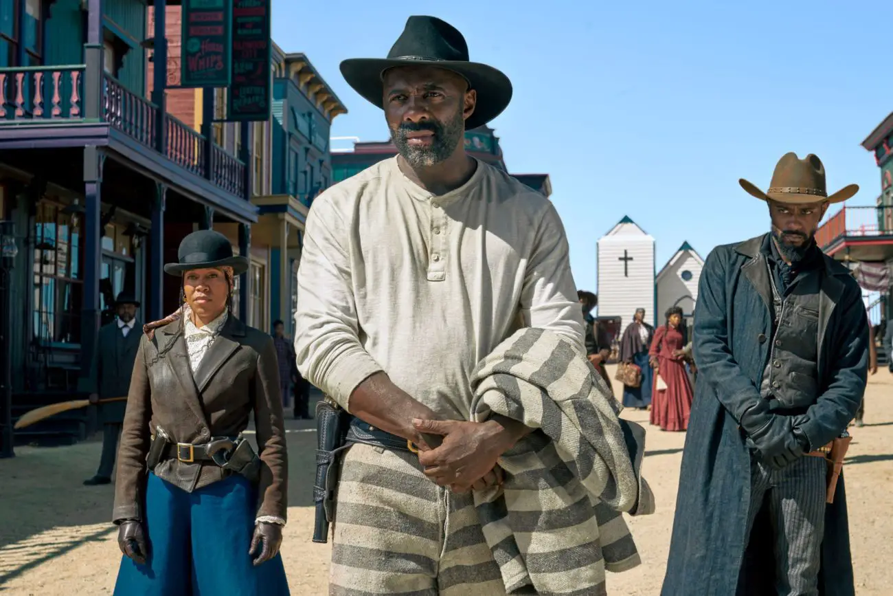 A man stands armed in a street and backed by two fellow outlaws.