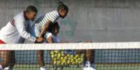 A man pushes a tennis ball cart with two girls.