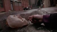 A mask lies on the pavement with a hand next to it in Vanilla Sky