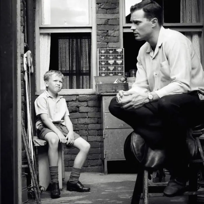 A boy sits listening to his father in an alley.