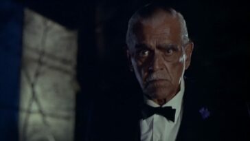 An older man with a white mustache wearing a black suit and bowtie stands in the darkness with a serious expression on his face (Boris Karloff in Peter Bogdanovich's film Targets)