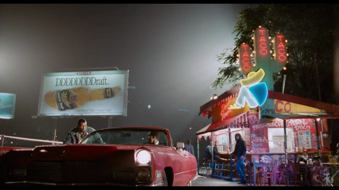 Image from Deep Cover: Stevens/Hull (Fishburne) and Eddie (Smith) in a parked car inn front of a brightly lit taco stand at night.