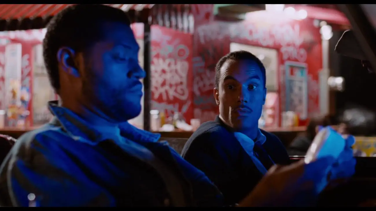Image from Deep Cover: While seated in a car and bathed in a neon blue light, Stevens/Hull and Eddie (Roger Guenveur Smith) inspect a packet of drugs.