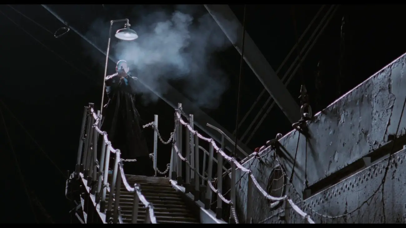 Image from Deep Cover: A man fires a weapon from the top of a staircase attached to a steamer at night, his discharge forming a cloud of smoke.