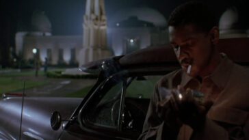 Image from Devil in a Blue Dress: Easy Rawlins (Denzel Washington) lights a cigarette outside his parked car at the Griffith Observatory at night, the characters of Daphne Monet (Jennifer Beals) and Todd Carter (Terry Kinney) in the background.