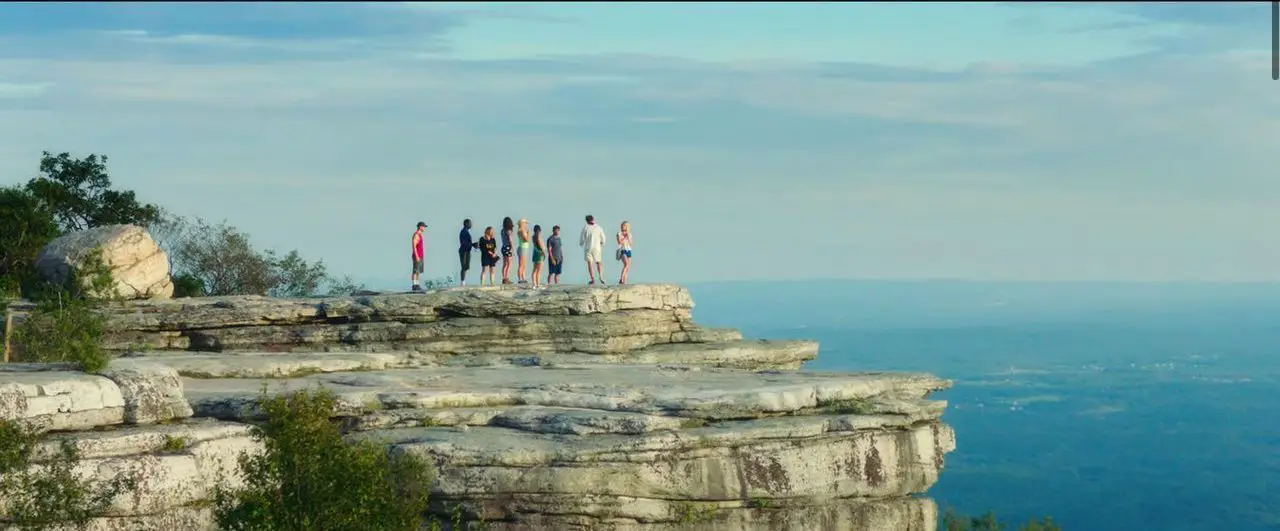 The group of attendees pause a hiking trip at an over looking cliff. 
