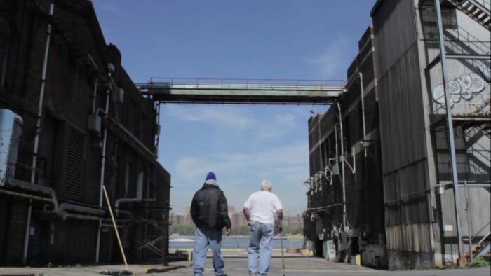 Screenshot from Third Shift, one of the short films added to Criterion Channel in November. Two men walk through a dilapidated factory. One is using a cane.
