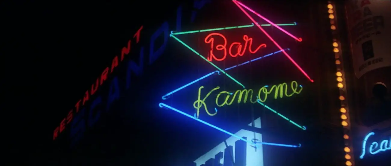 Image from Tokyo Drifter: A neon sign reading "Bar Kamome" is lit in blue, red, and green against a black background and several triangular shapes.