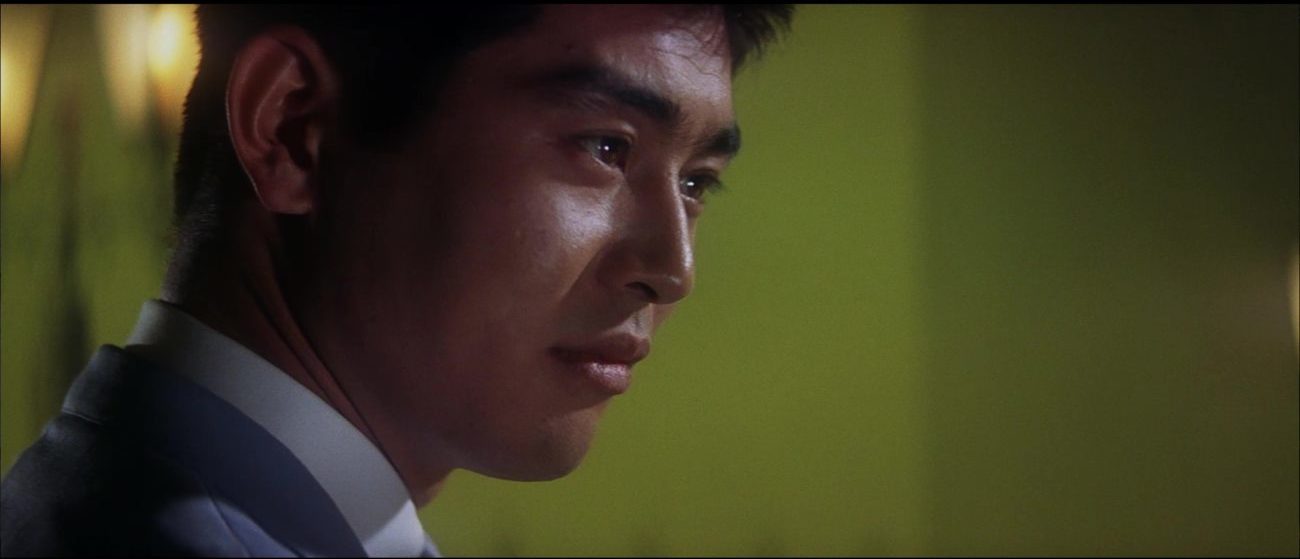 Image from Tokyo Drifter: Tetsu is shown in close-up, staring to camera right in front of a lime-green background.