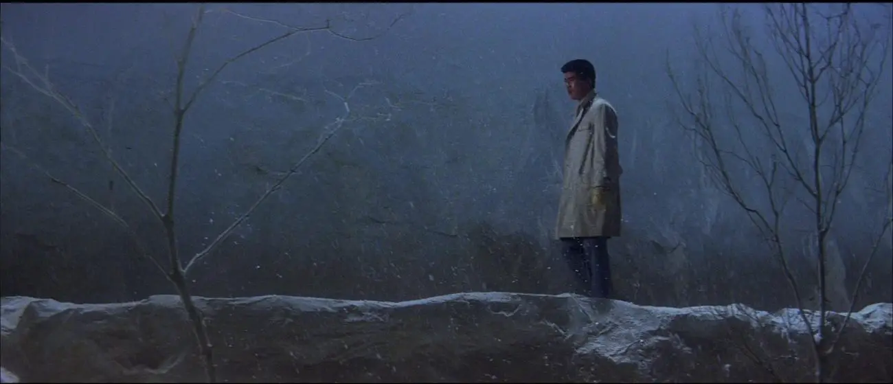 Image from Tokyo Drifter: Tetsu is depicted wandering in long shot against a snowy blue background.