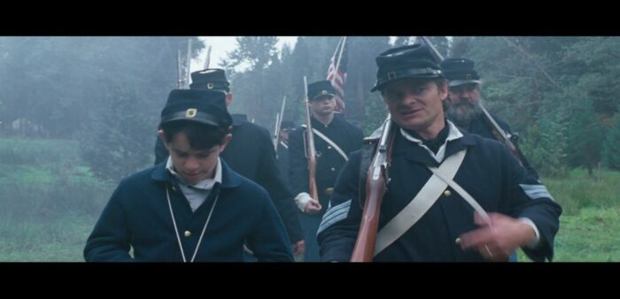 Greg (left) and Frank (right) dressed in 1800s American army uniforms marching along a foggy forest path, other war reenactors behind them.