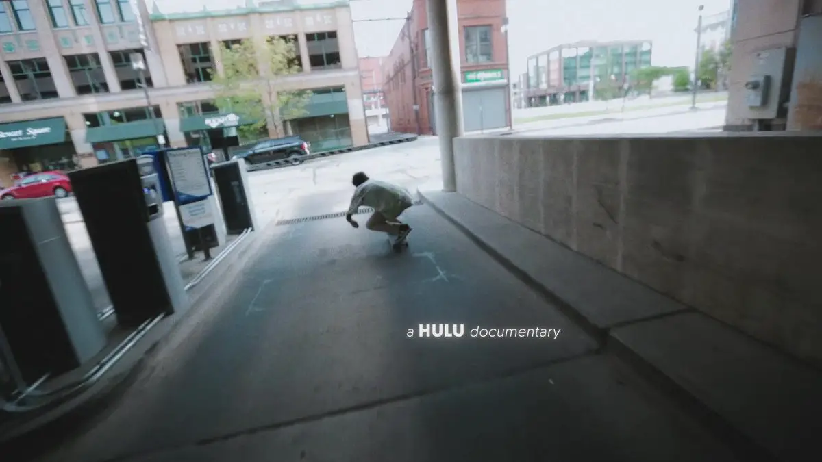 Image from Minding the Gap: A skateboarder ducks under the exit gate of a concrete parking ramp.