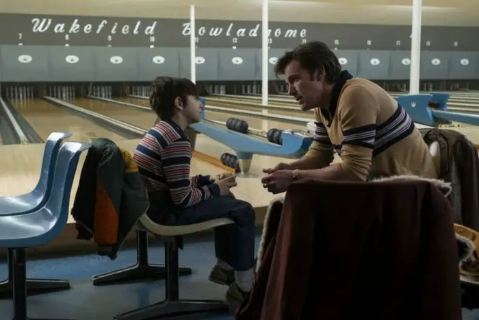 A young boy and a man talk at a bowling alley.