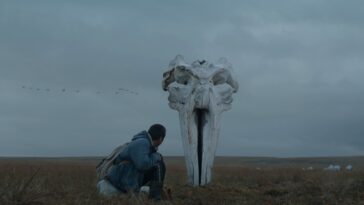 Leshka, the film's main character, kneels before the skull of a whale planted upright in the ground.