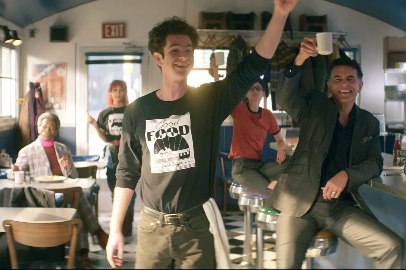Jon (Andrew Garfield) standing in the Moondance Diner with his arm raised, with Carolyn (MJ Rodriguez) and three diners (André de Shields, Beth Malone, and Brian Stokes Mitchell) standing behind him in various poses.