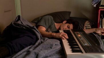 Jon (Andrew Garfield) lying on his side in bed, one hand resting on a keyboard lying next to him.