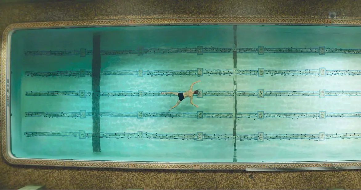 Overhead view of Jon (Andrew Garfield) floating in a pool, with sheet music superimposed underneath.