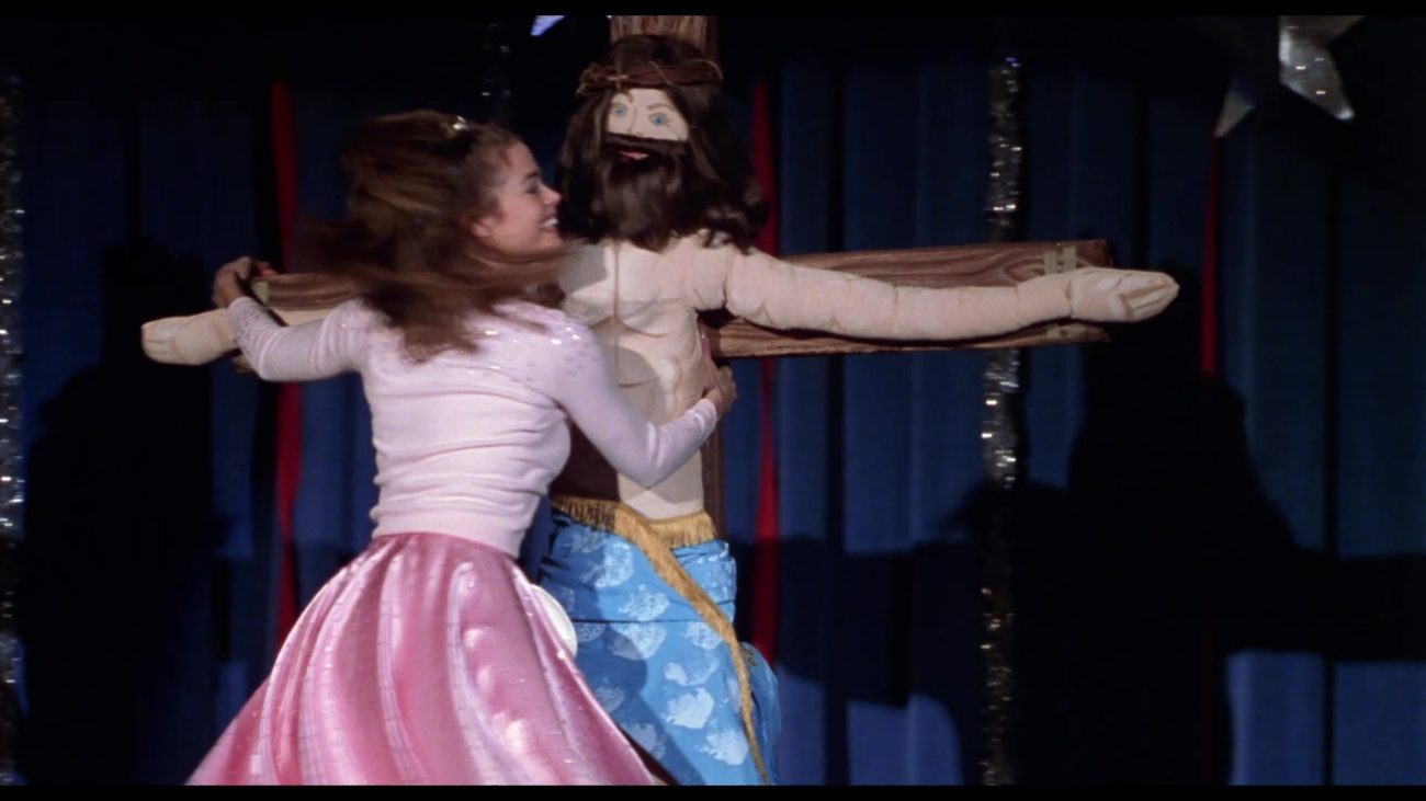 Denise Richards as Becky Ann Leeman dances with an effigy of Jesus Christ on the cross in a scene from Drop Dead Gorgeous.