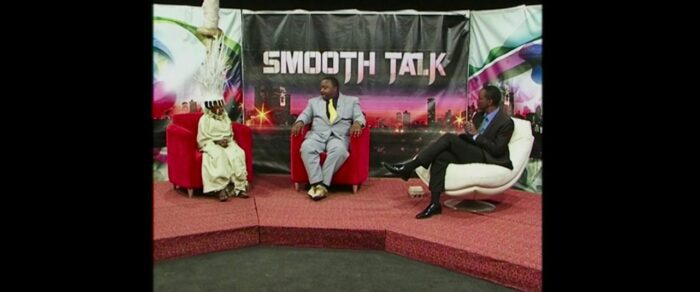 Two men in suits and little girl in traditional African costume in TV studio