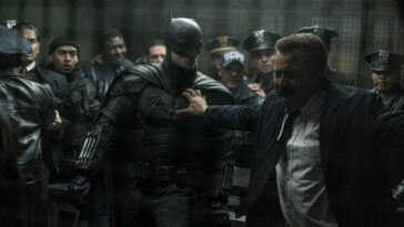 A suited police officer holds back Batman from a fight.