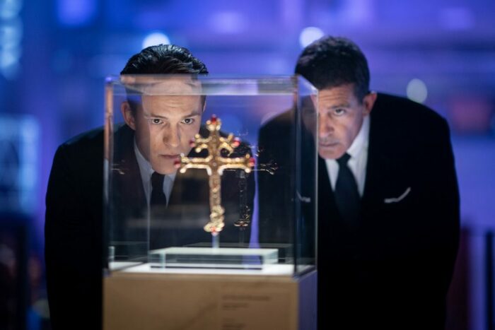 Two men look at an encased golden cross key.